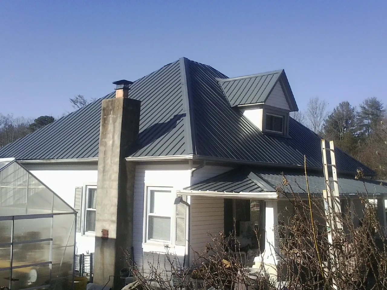 Dark blue standing seam metal roof on a white farmhouse with dormer — Slate & Tile Roof Repair by Roofing Brothers in Dietrich