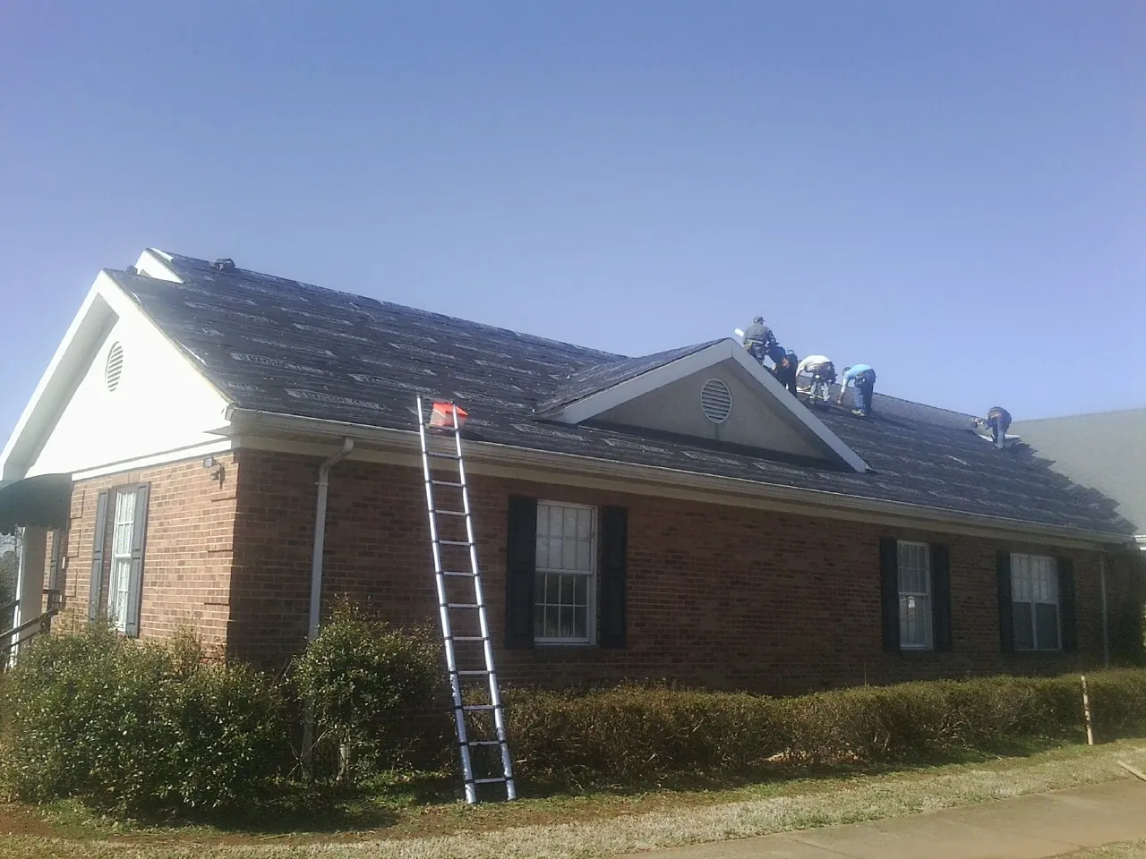 Crew tearing shingles off a brick ranch roof with a ladder set — Emergency Roof Repair work by our crew in Dietrich