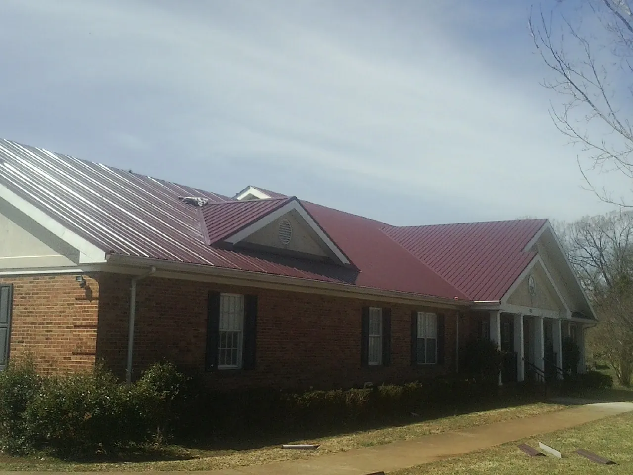 Red metal roof with gabled entries on a long brick building, from a Hail Damage Roof Repair job in Dietrich