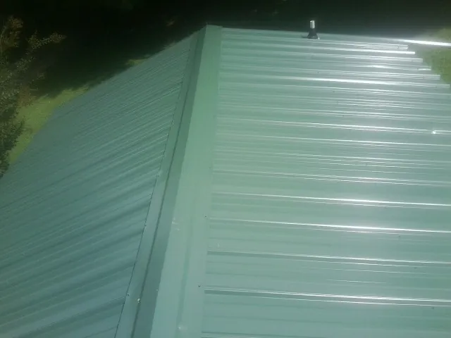 New green metal panels meeting at the ridge of a roof — Flat Roof Repair work by our crew in Dietrich
