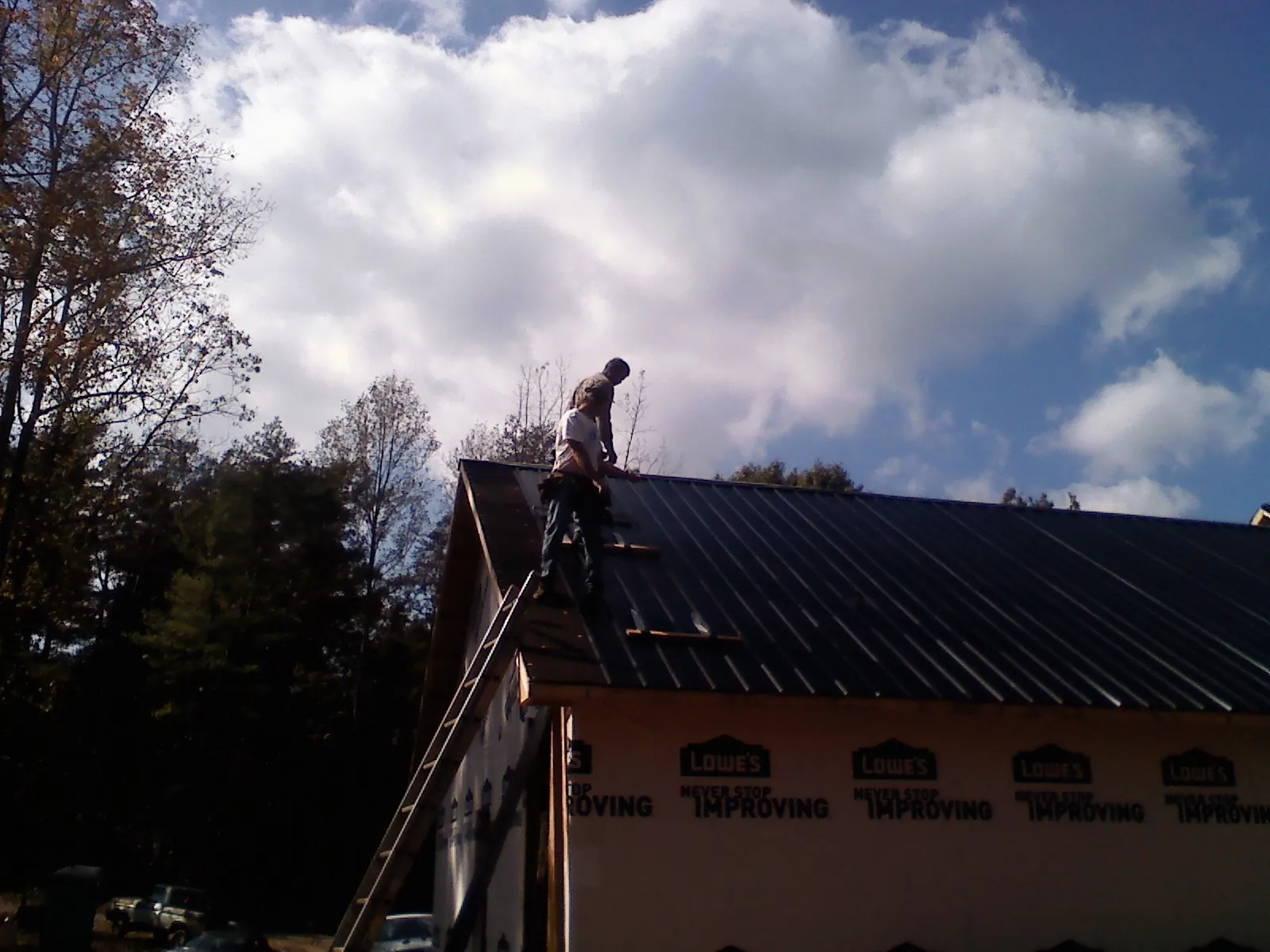 Roofer fastening dark metal panels high against a cloudy sky, from a Roof Inspection job in Dietrich