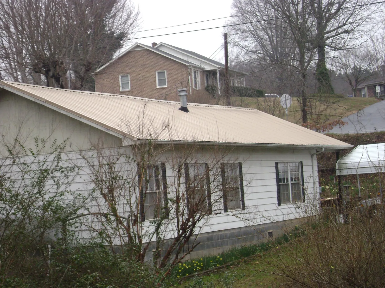 Tan metal roof on a white sided house set into a hillside — Commercial Roofing by Roofing Brothers in Dietrich